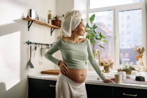 Future maman dans sa cuisine, main posee sur son ventre rond, lumiere naturelle du matin