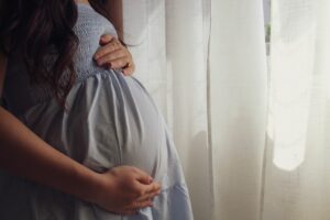 Future maman caressant son ventre près d'une fenêtre, moment doux pour porter son bola de grossesse