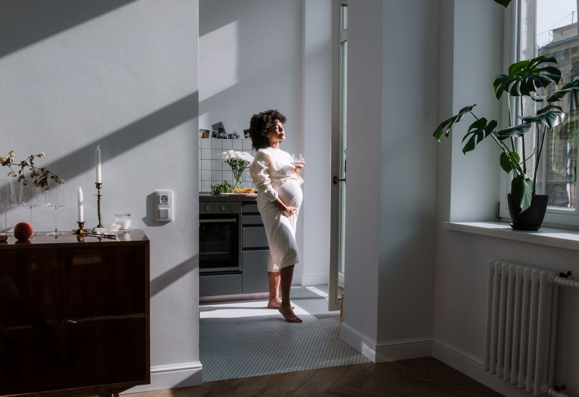 Femme enceinte souriante dans une cuisine ensoleillée, portant un bola de grossesse